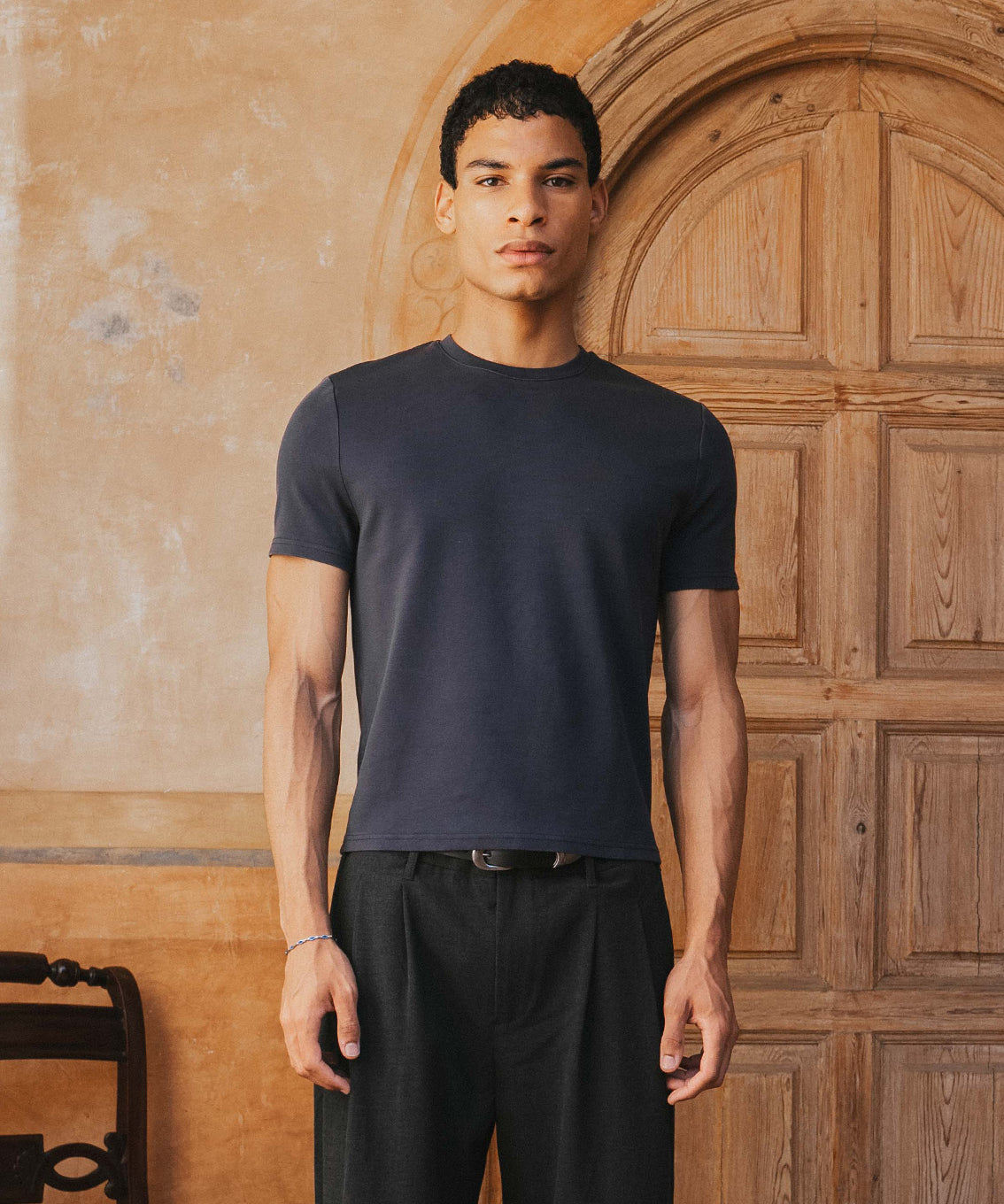 Man wearing a black t-shirt and pants standing in front of a wooden door.