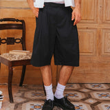 Person wearing black shorts and white shoes standing on a patterned floor with wooden paneling.